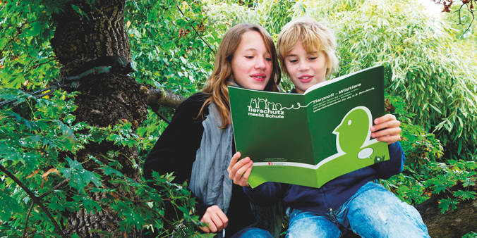 zwei Kinder mit großem Buch unter einem Baum